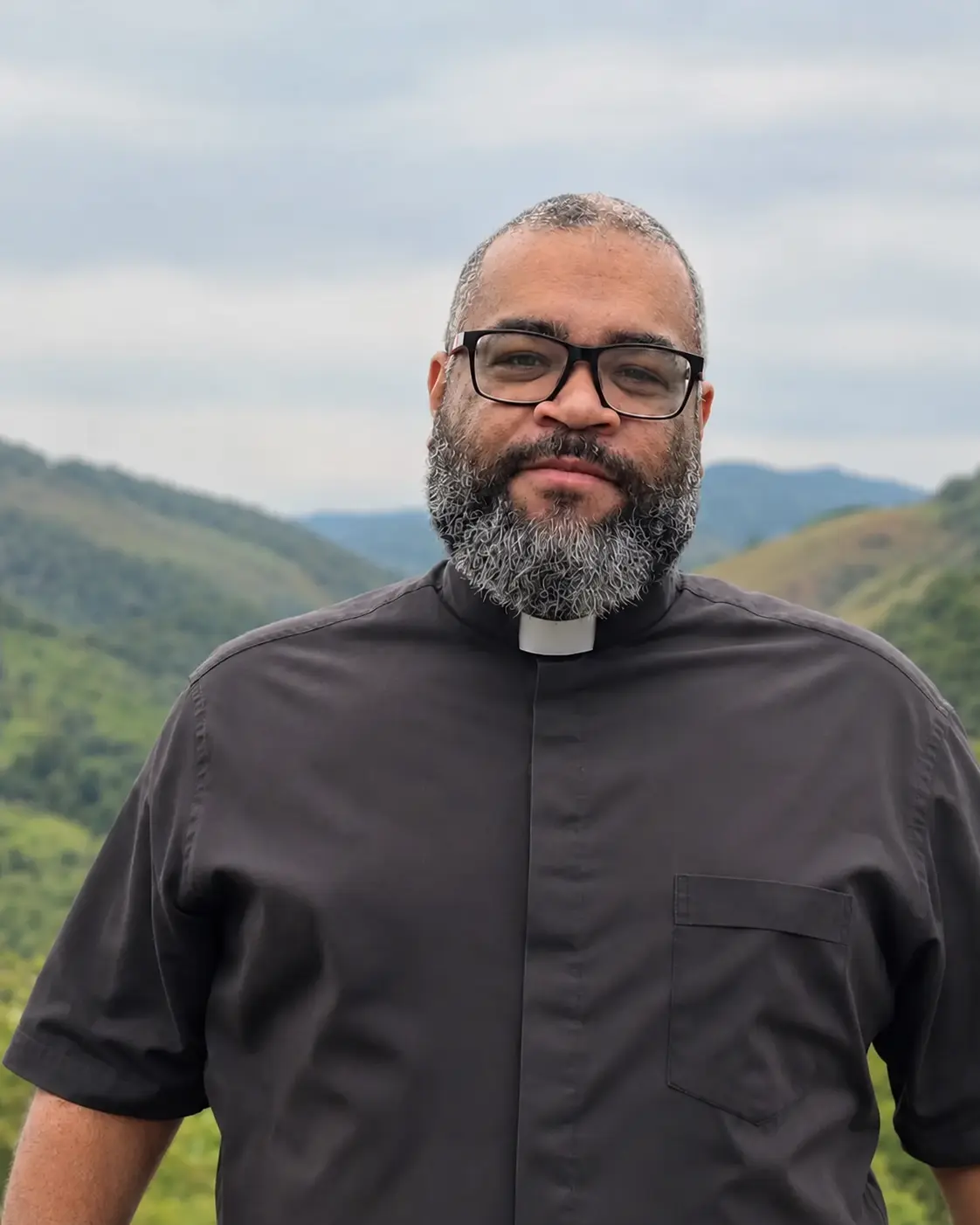 Pe. Luis Claudio Cruz com traje clerical diante de uma paisagem de montanhas